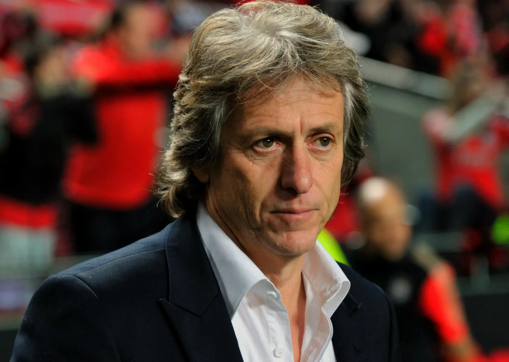 Retrato do treinador de futebol Jorge Jesus vestindo paletó escuro e camisa branca.